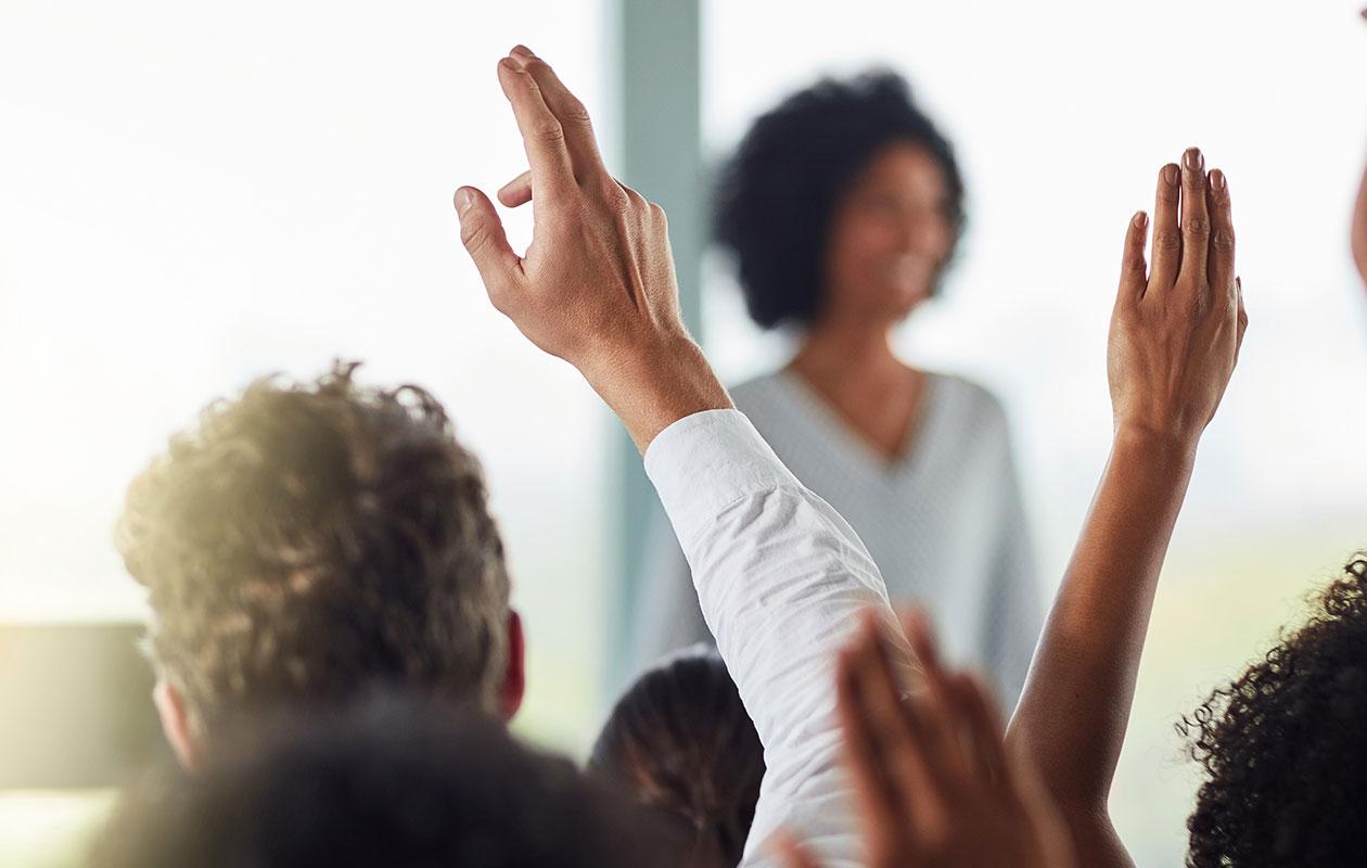 Business people and hands raised for questions at conference