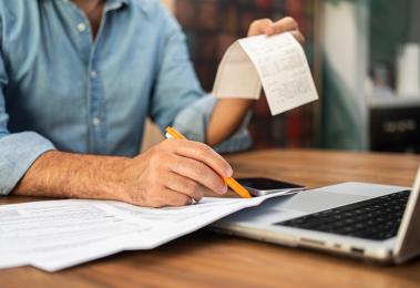 Man filling out tax forms at home using a laptop and holding receipts.